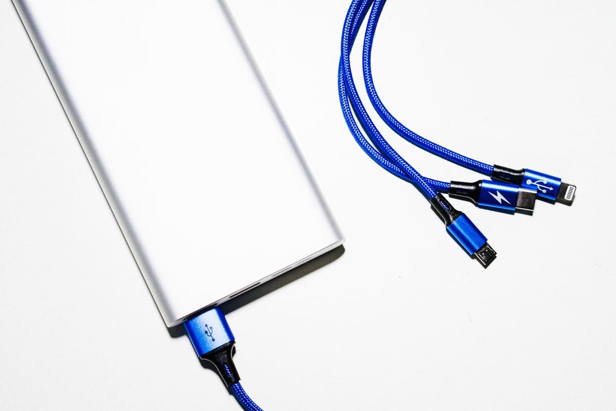 Silberne Powerbank auf weißem Untergrund, daneben ein blaues Mehrfachladekabel mit drei Steckern