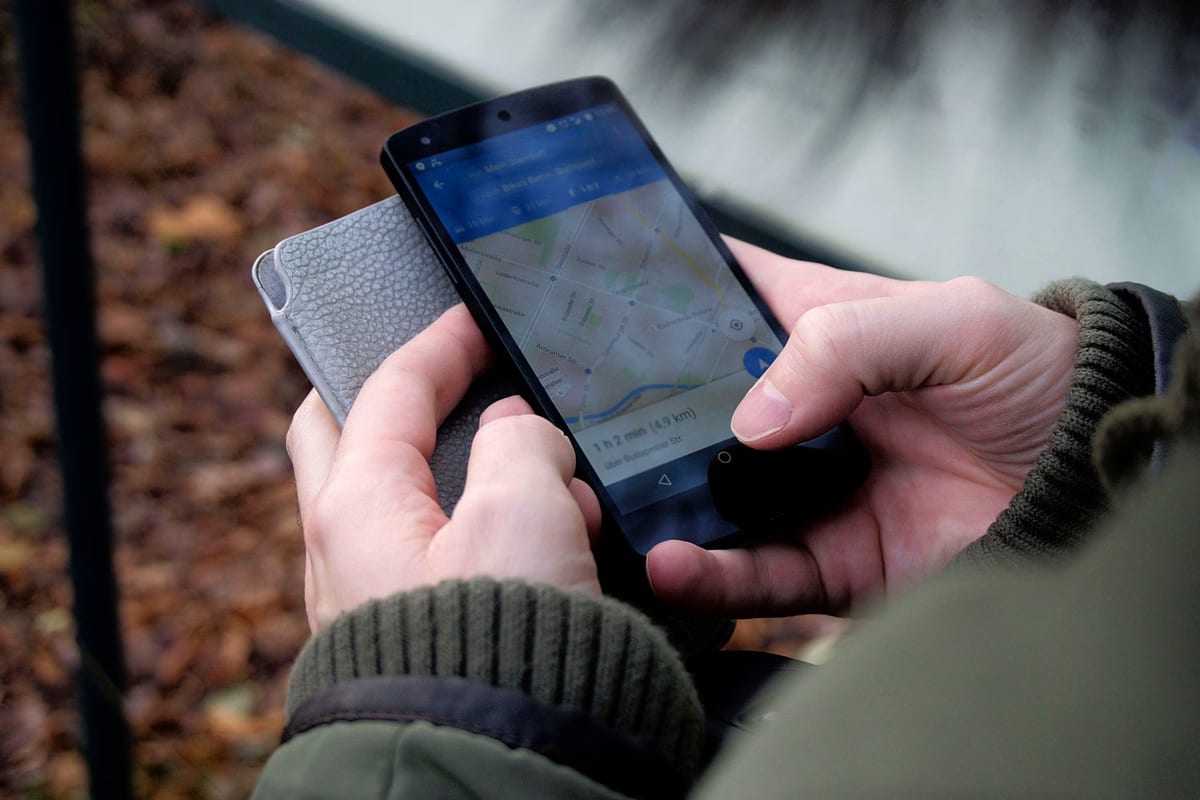 Hände halten ein Smartphone mit geöffneter Kartenansicht und eingezeichneter Route, im Hintergrund Herbstlaub