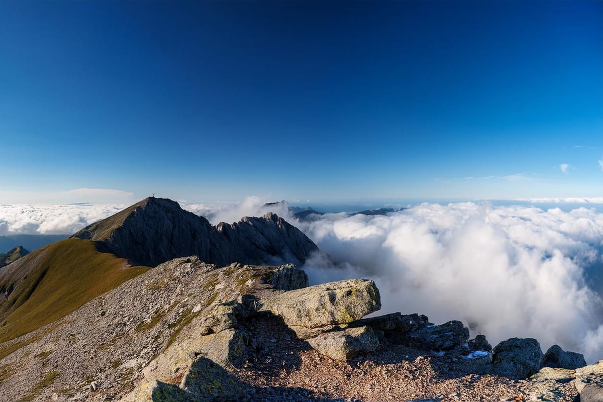 Felsgrat oberhalb eines geschlossenen Wolkenmeers, darüber tiefblauer Himmel