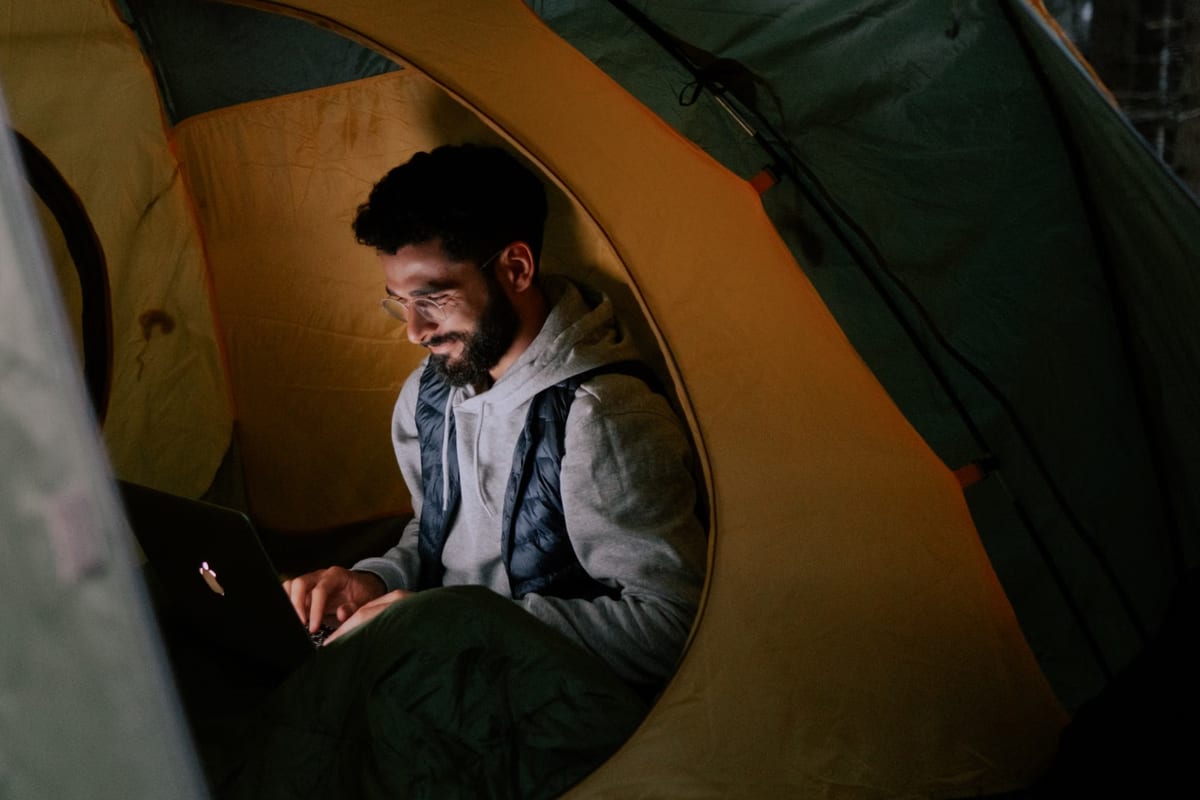 Person sitzt abends im beleuchteten Zelt und arbeitet an einem aufgeklappten Laptop