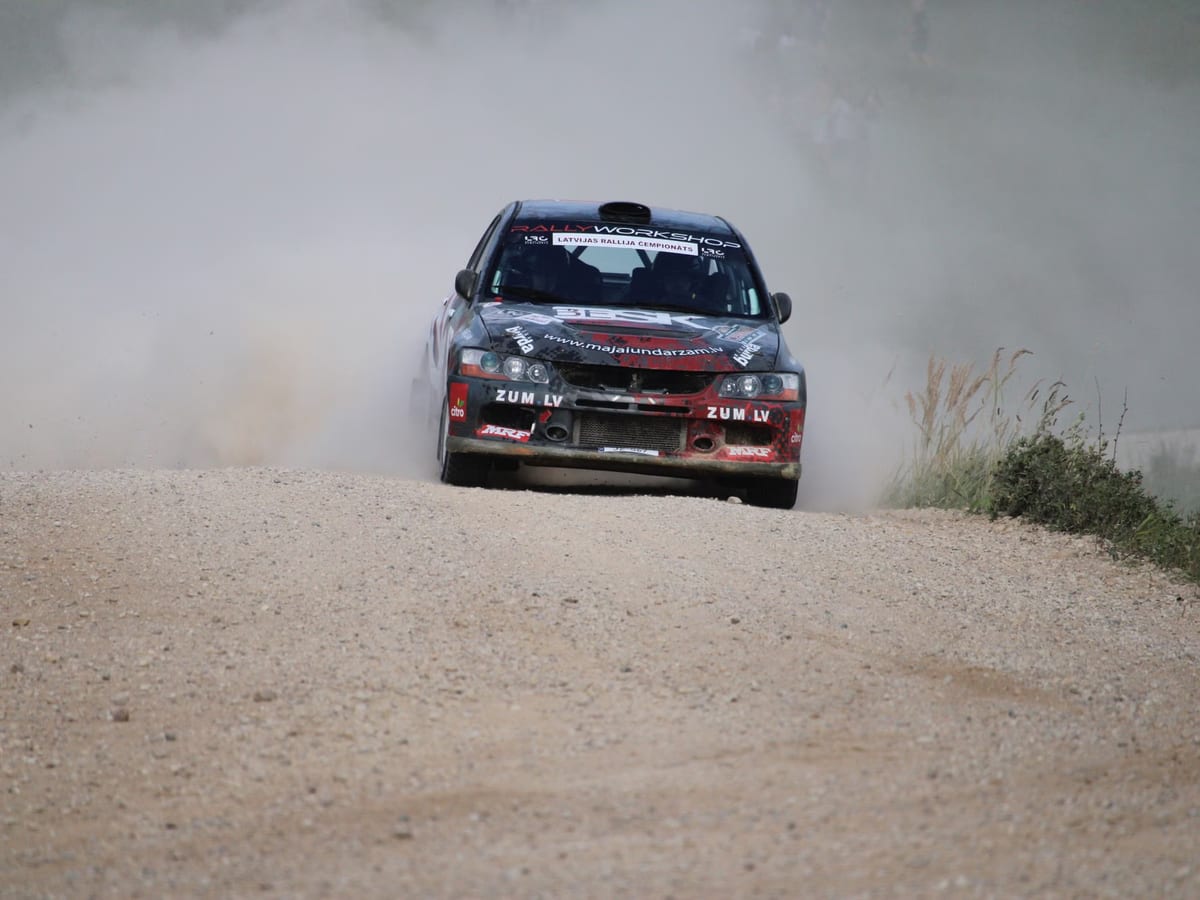 Rallyefahrzeug auf einer Schotterpiste, das eine dichte Staubfahne hinter sich herzieht